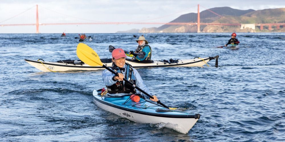 A group of people are paddling kayaks in the ocean.