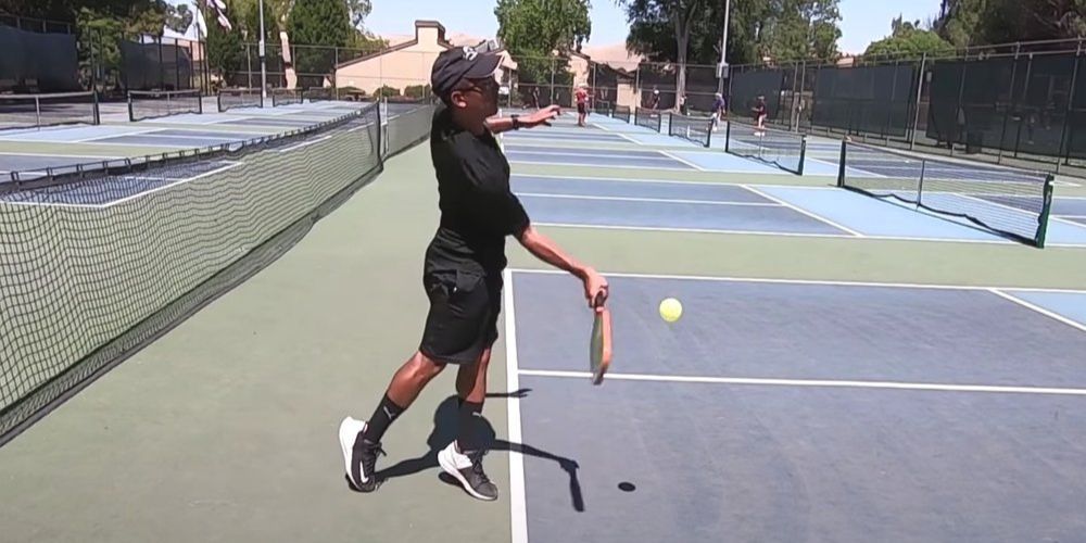 A man is swinging a pickleball paddle at a pickleball ball