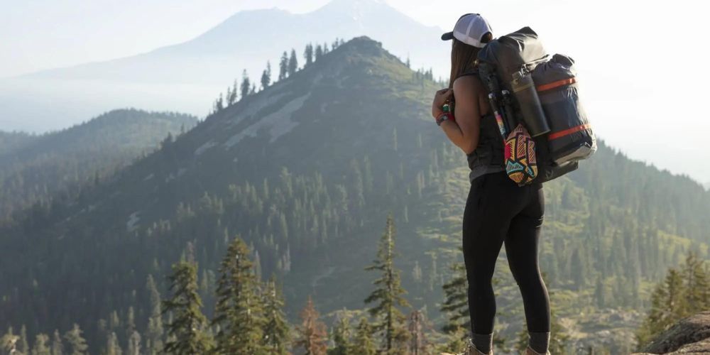 A woman with a backpack is standing on top of a mountain.