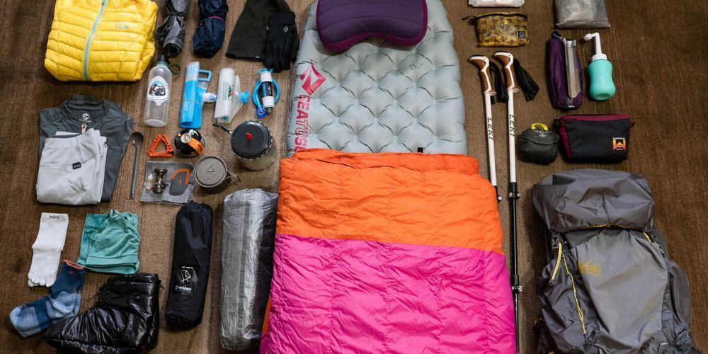 A sleeping bag is surrounded by a variety of camping gear on a wooden table.