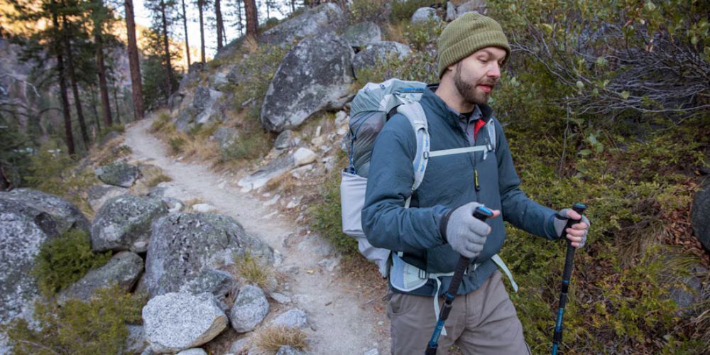 A man with a backpack is walking down a trail in the woods.