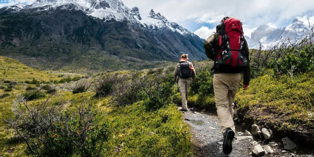 Two people with backpacks are walking down a path in the mountains.