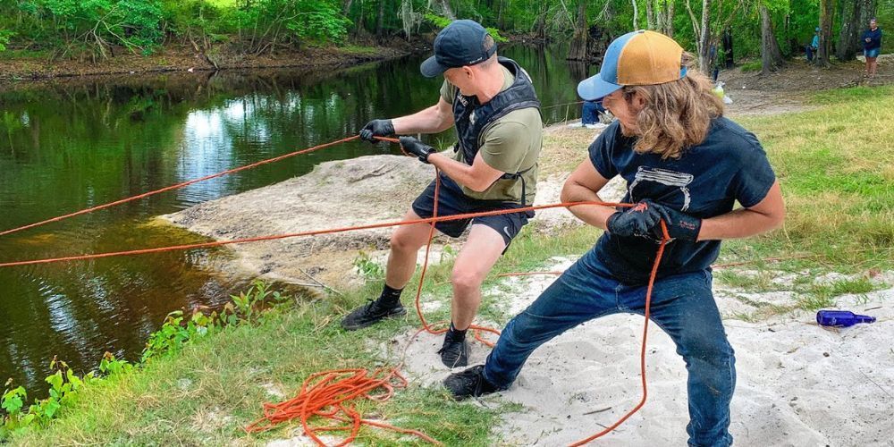 Two men are pulling a rope towards a body of water.