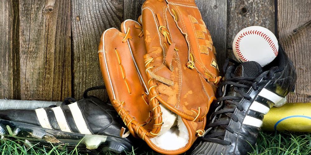 A baseball glove , bat , cleats , and a baseball are on a wooden table.