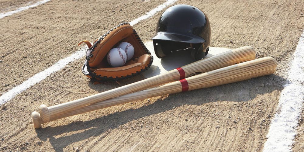 A baseball helmet , glove , bats and ball are on a baseball field.