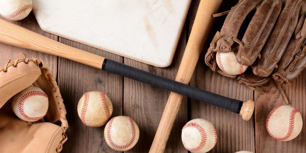 A wooden table topped with baseballs , bats , gloves and a base.