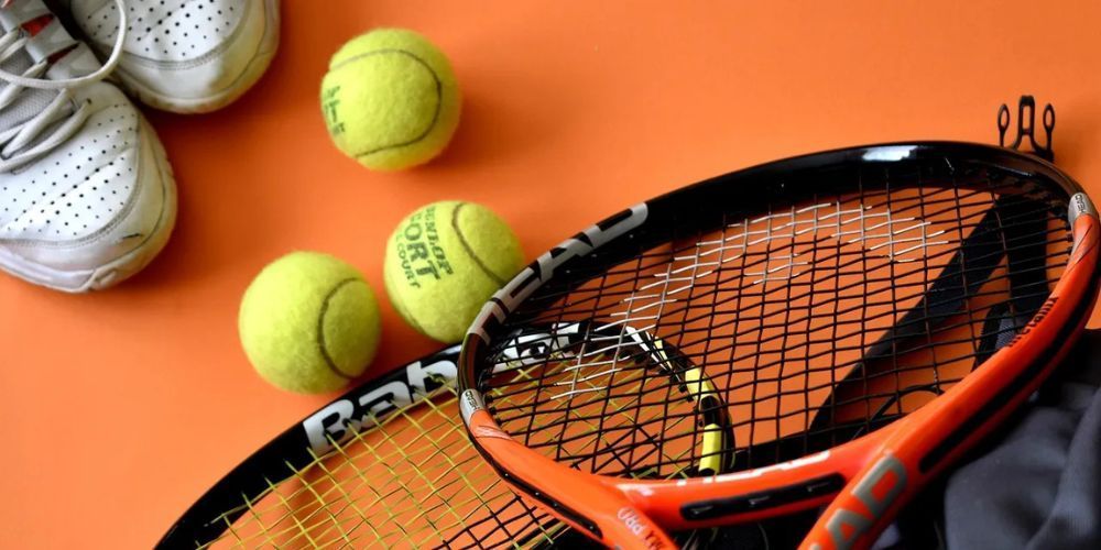 A tennis racket and tennis balls on an orange surface