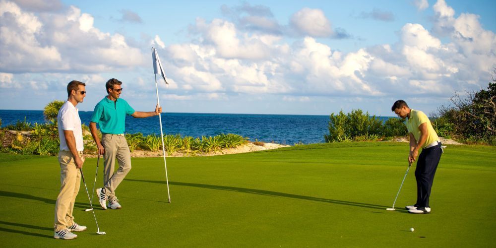 Three men are playing golf on a golf course with the ocean in the background.