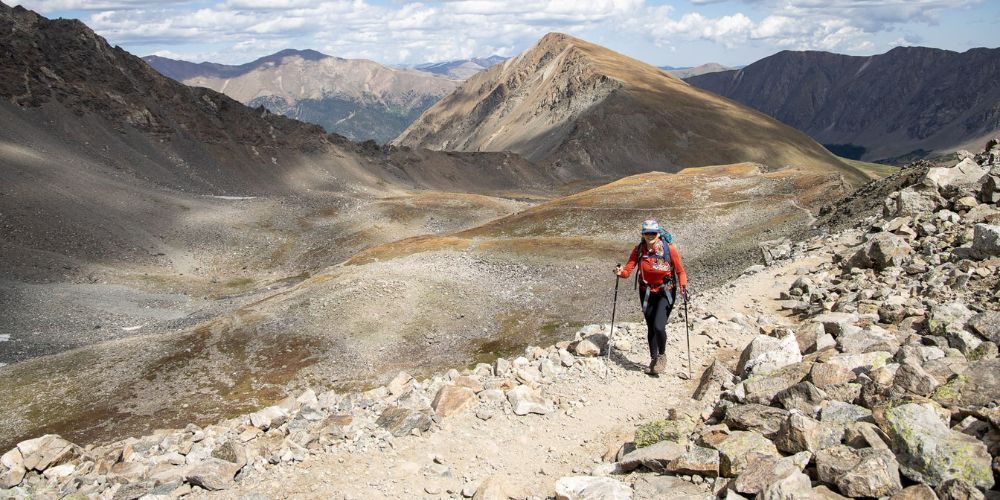 A person with a backpack is walking on a rocky trail in the mountains.