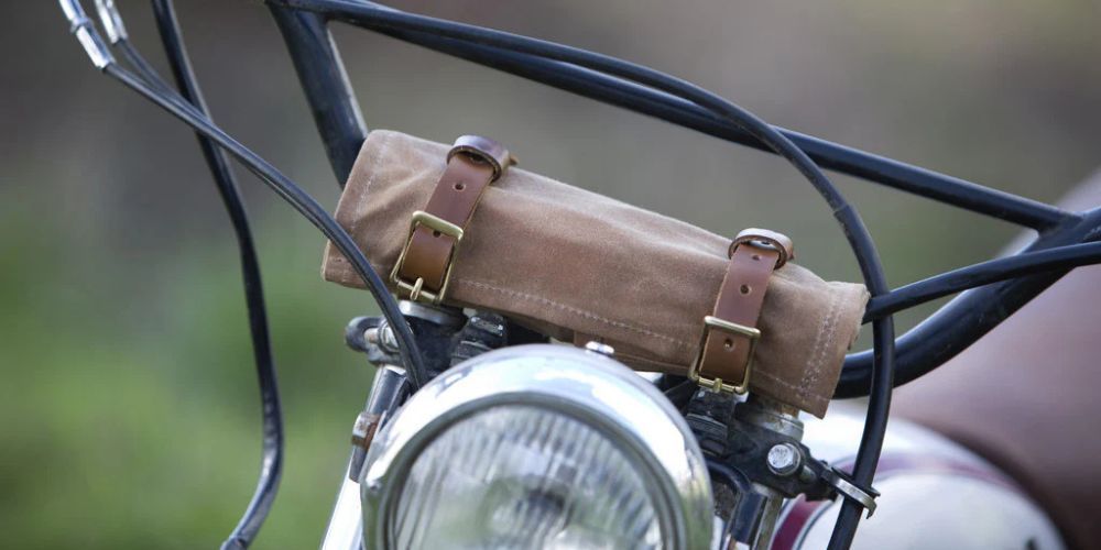 A close up of a motorcycle with a leather bag on the handlebars.