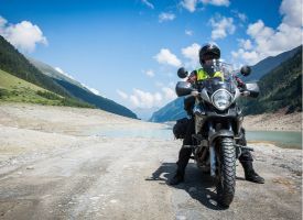A man is standing next to a motorcycle on a dirt road.