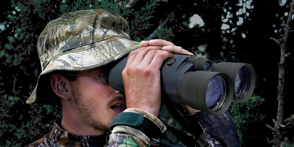 A man in a camo hat is looking through binoculars.