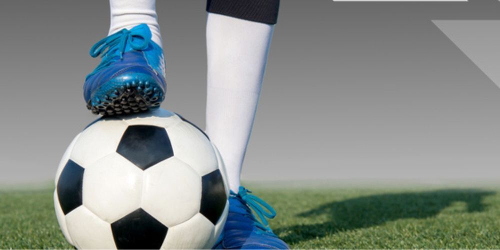 A person is standing on top of a soccer ball on a field.