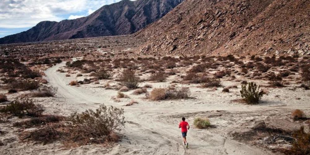 A man in a red shirt is running on a dirt road in the desert.