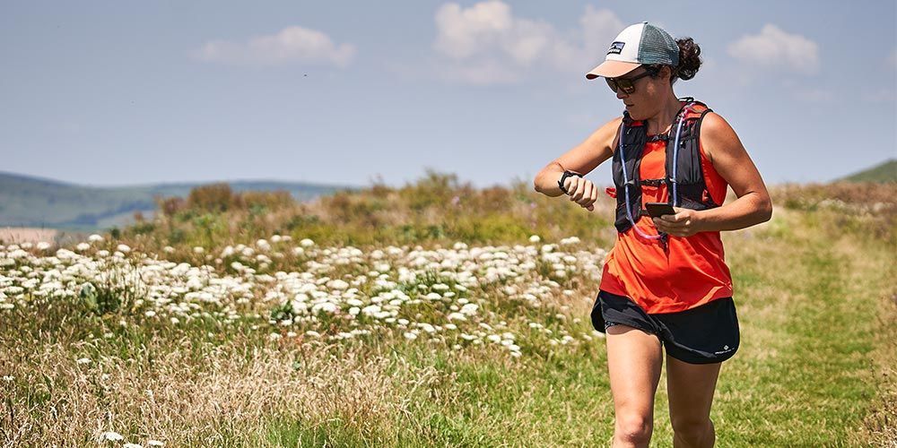 A woman is running through a field of flowers and checking her watch.