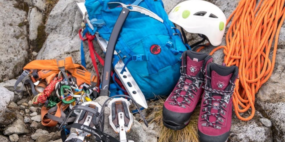 A pair of climbing boots , a helmet , a rope , and a backpack are sitting on a rock.