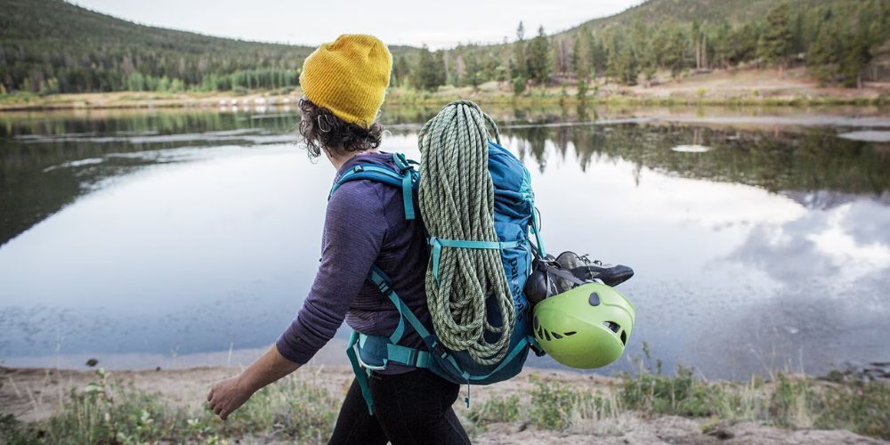 A woman with a backpack is walking towards a lake.