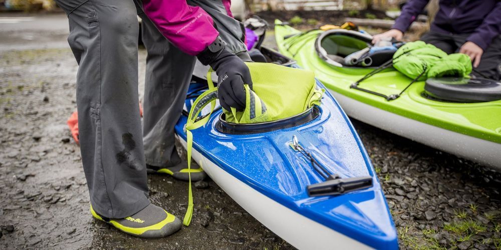 A person is standing next to a blue and green kayak.