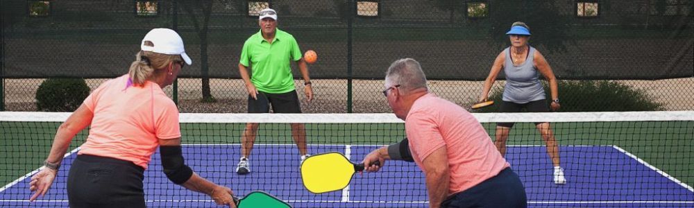 A group of people are playing a game of pickleball on a tennis court.