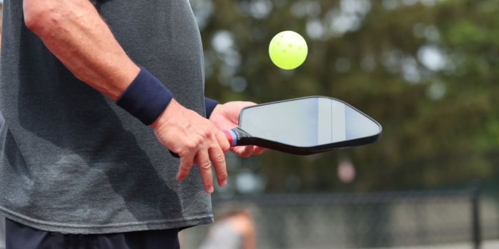 A man is holding a paddle and a pickleball ball.