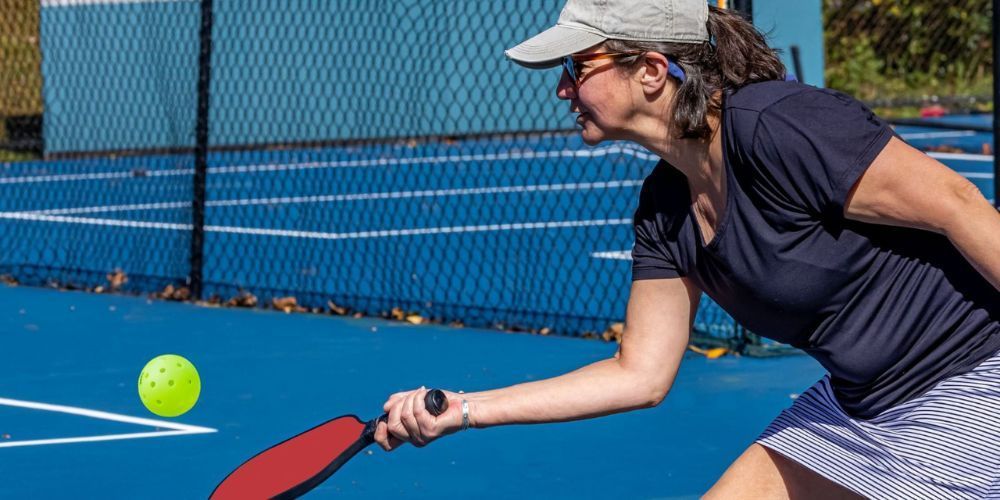 A woman is playing pickleball on a blue tennis court.