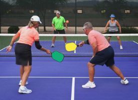 A group of people are playing a game of pickleball on a tennis court.