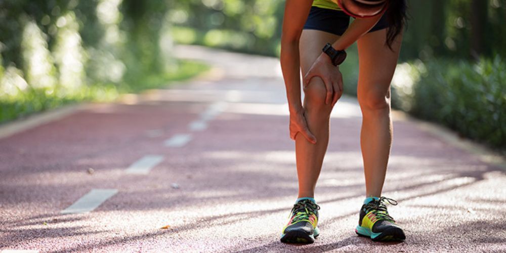 A woman is holding her knee in pain while running on a track.