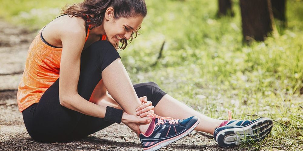 A woman is sitting on the ground holding her ankle in pain.