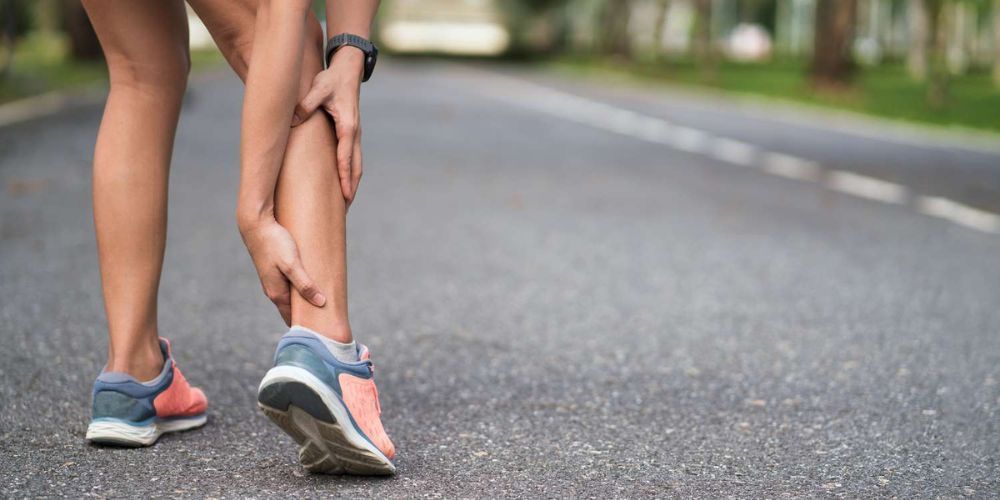 A woman is holding her ankle in pain while running on a road.