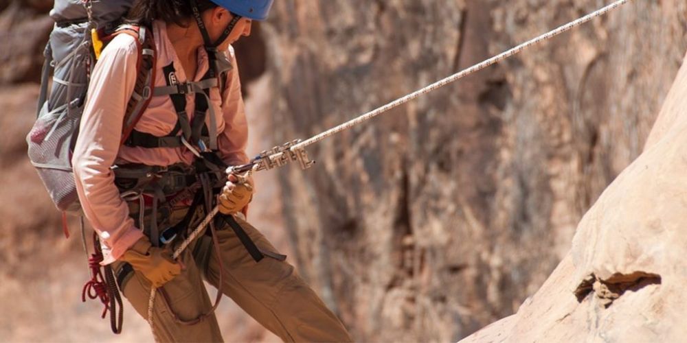 A woman with a backpack is holding onto a rope while climbing a mountain.