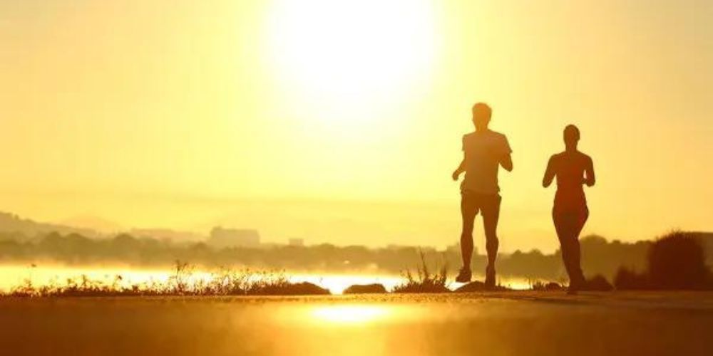 Two people are running on a beach at sunset.