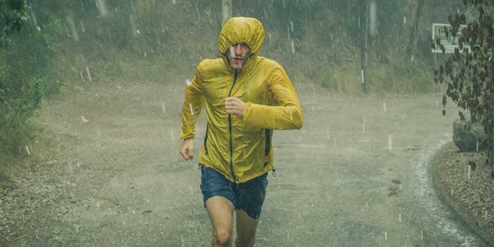 A man in a yellow jacket is running in the rain.