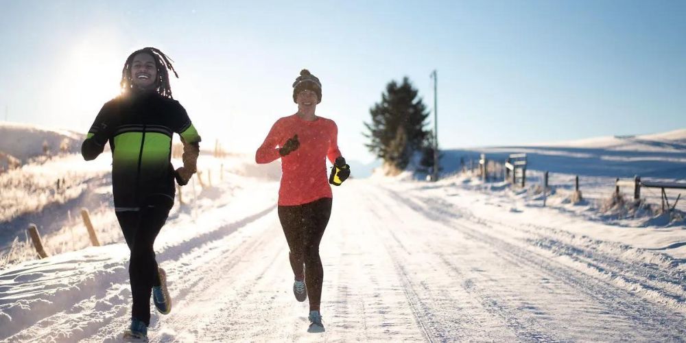 A man and a woman are running on a snowy road.