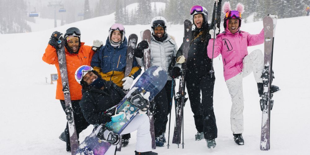 A group of people are standing in the snow holding skis and snowboards.