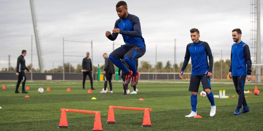 A group of soccer players are jumping over cones on a field.