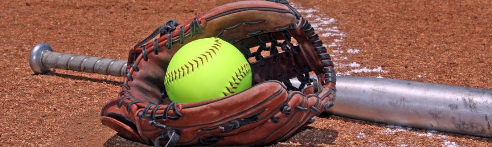 A softball in a glove next to a bat on a baseball field.