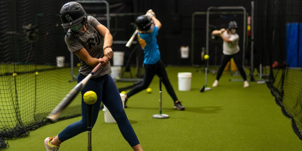 A group of young girls are practicing baseball in a cage.