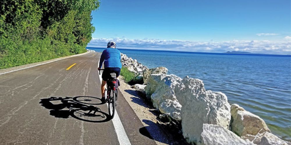 A man is riding a bike down a road next to a body of water.