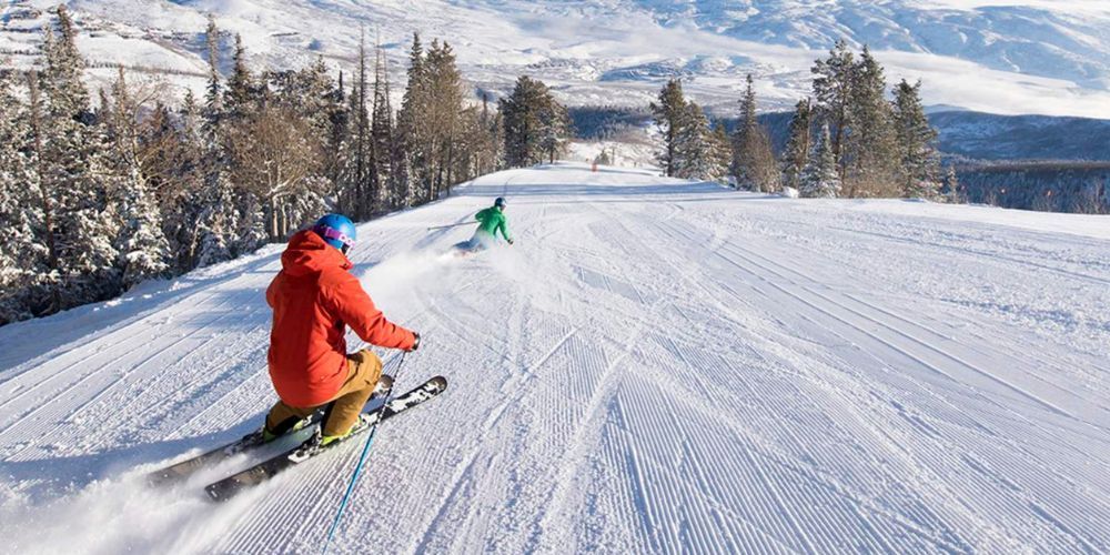 Two people are skiing down a snow covered slope.