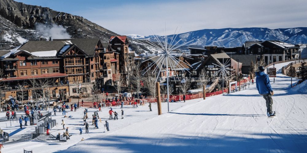 A man is skiing down a snow covered slope in a ski resort.