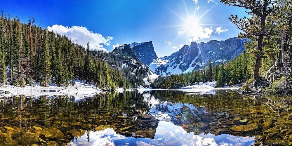 There is a lake in the middle of a forest with mountains in the background.