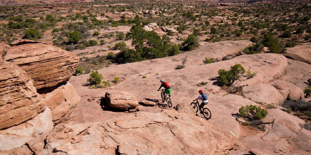 Two people are riding bikes on a rocky trail in the desert.