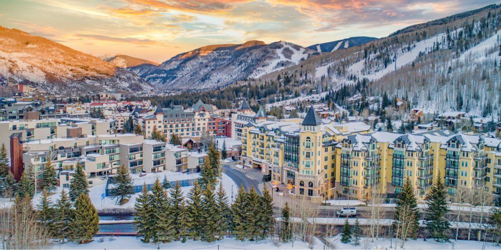 An aerial view of a ski resort surrounded by snow covered mountains at sunset.