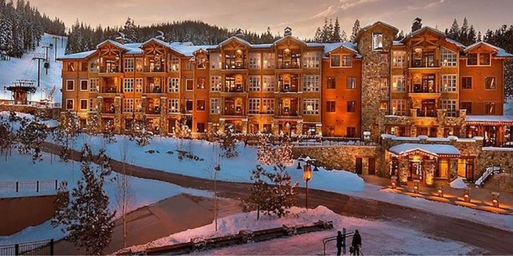 A large building with a lot of windows is surrounded by snow and trees.