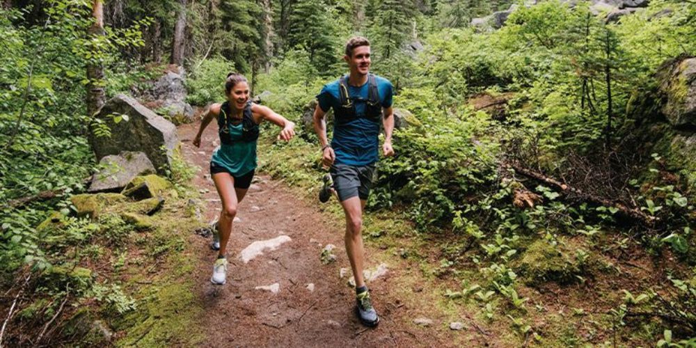 A man and a woman are running on a trail in the woods.