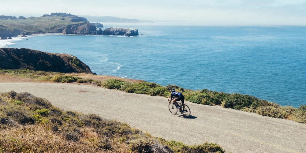 A man is riding a bike down a dirt road near the ocean.