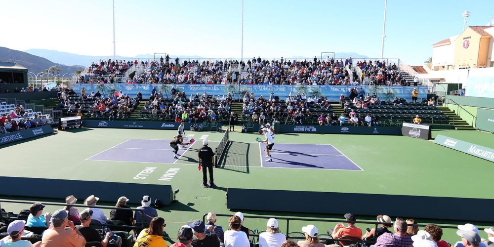 A crowd of people are watching a pickleball match on a court.