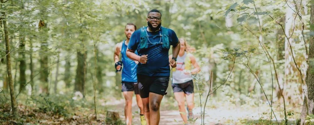 three people running on a trail in the woods