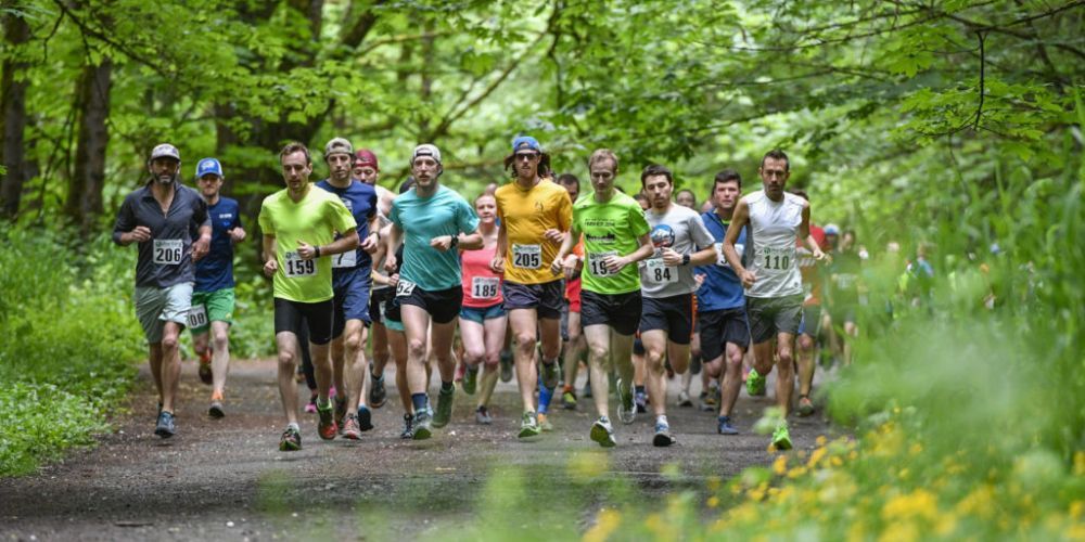 A group of people are running down a path in the woods.