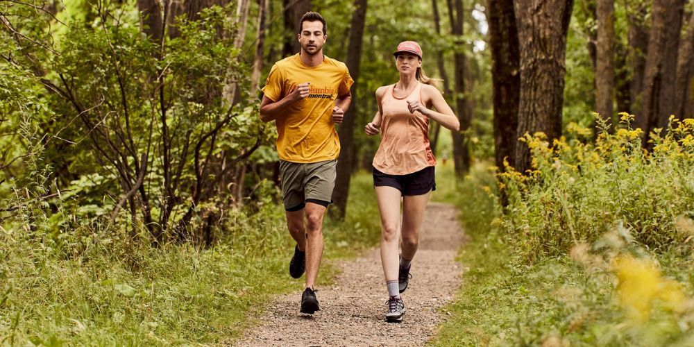 A man and a woman are running on a path in the woods.